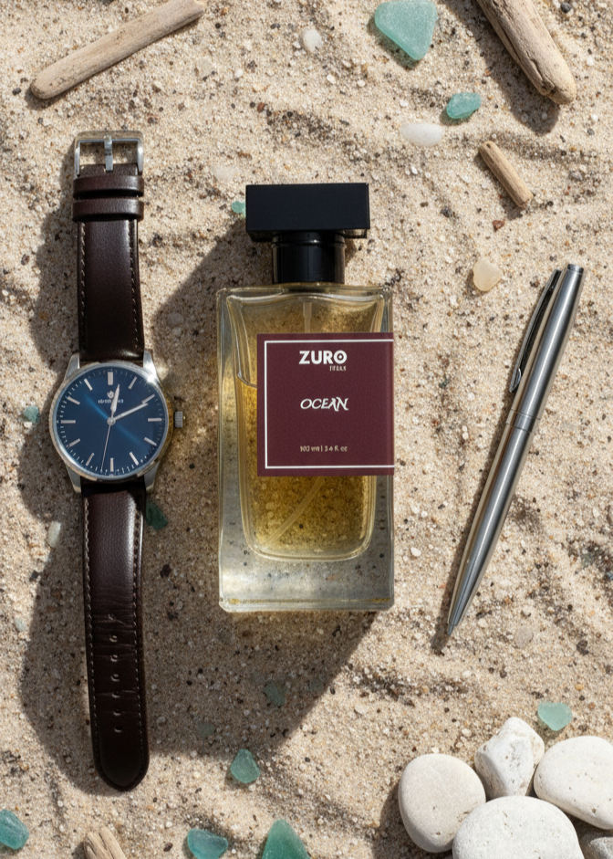 Watch, perfume bottle, and pen on a sandy surface with pebbles